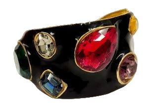 A black cuff bracelet featuring multiple colorful faceted gemstones in gold-toned bezel settings, including a prominent red stone, a pink stone, a blue stone, and a green stone.